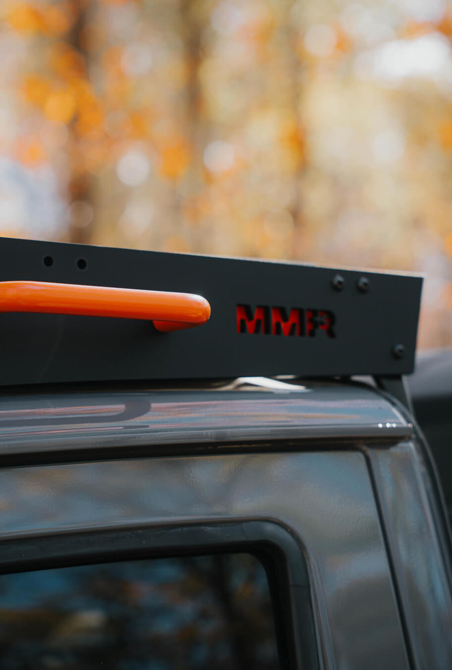 Roof rack with orange handle and 'MMR' branding on a vehicle, blurred natural background