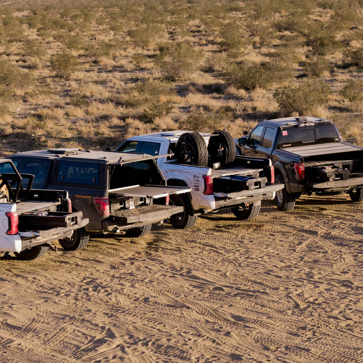 The four Optima trucks parked next to each other with their truck beds open, revealing the critical DECKED system setups inside.