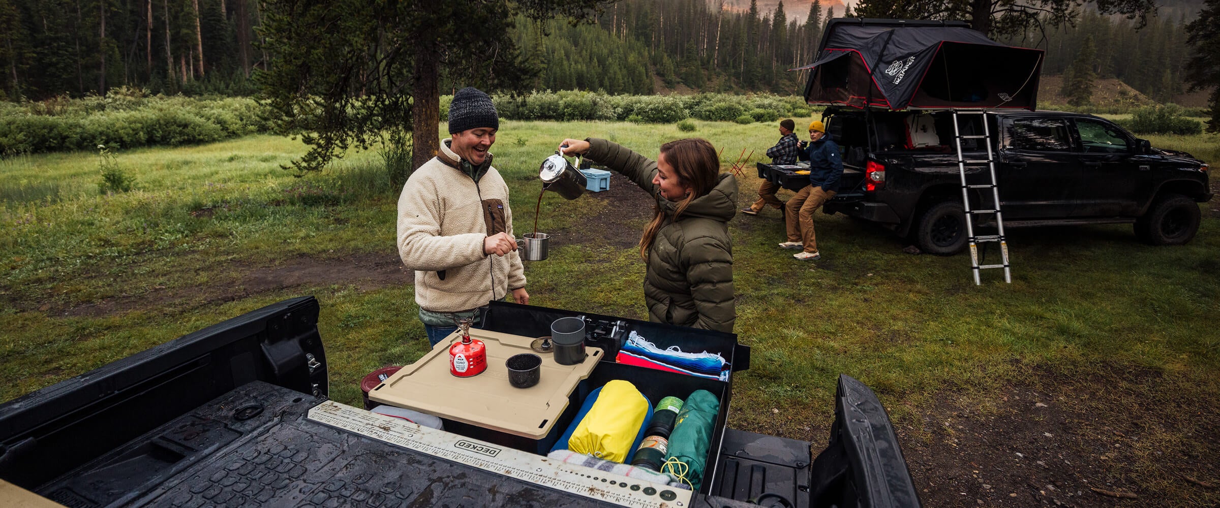 Decked employees at a campsite pouring coffee for each other, using the drawer system as a tabletop.