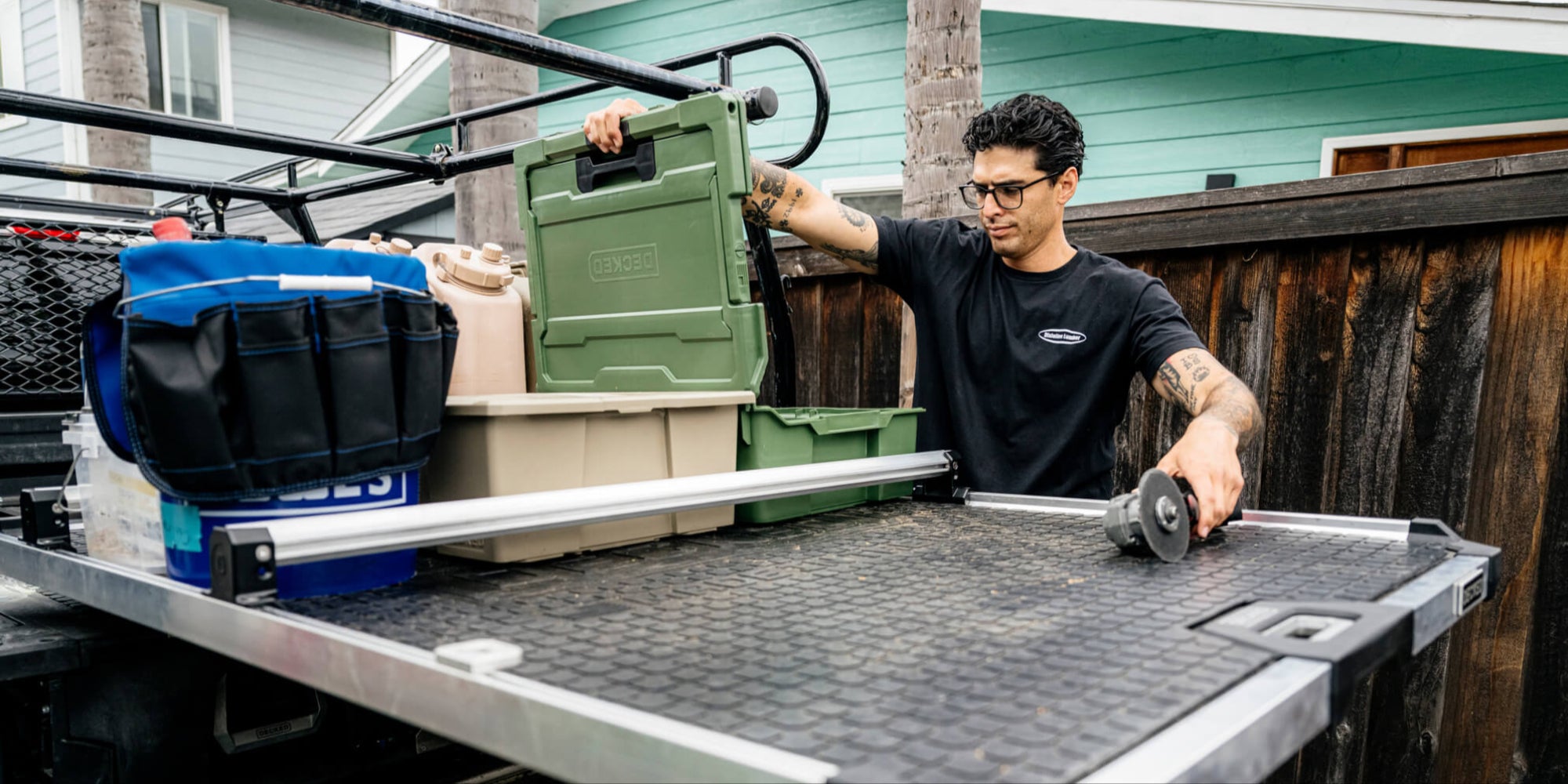 A man loading gear into his DECKED D-co Case. His cases, tool buckets and other bins are gently secured to the tray of his CargoGlide by his Crossbars.