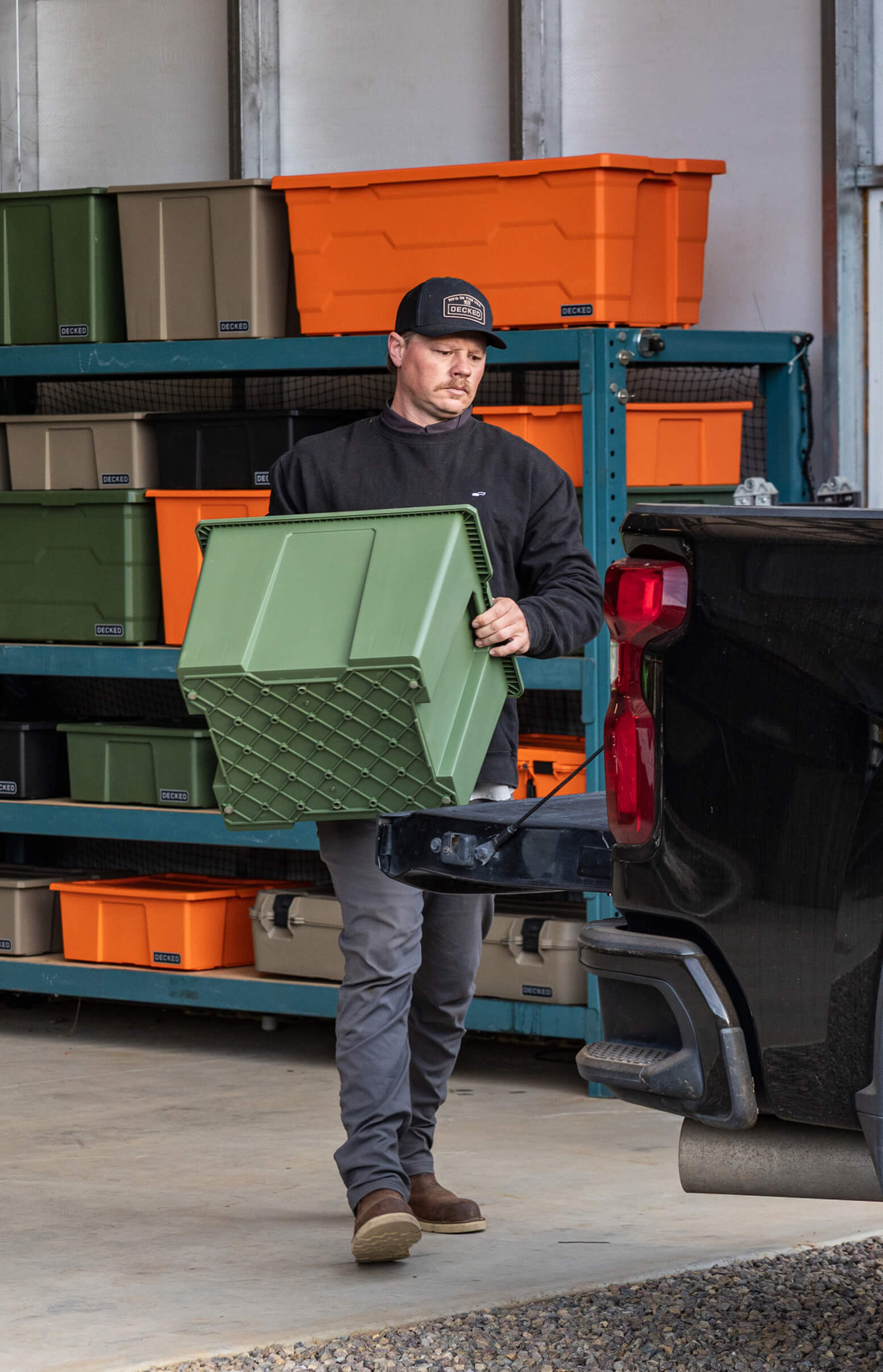 Man loading a green Payloader 64 storage bin onto a truck in a warehouse setting