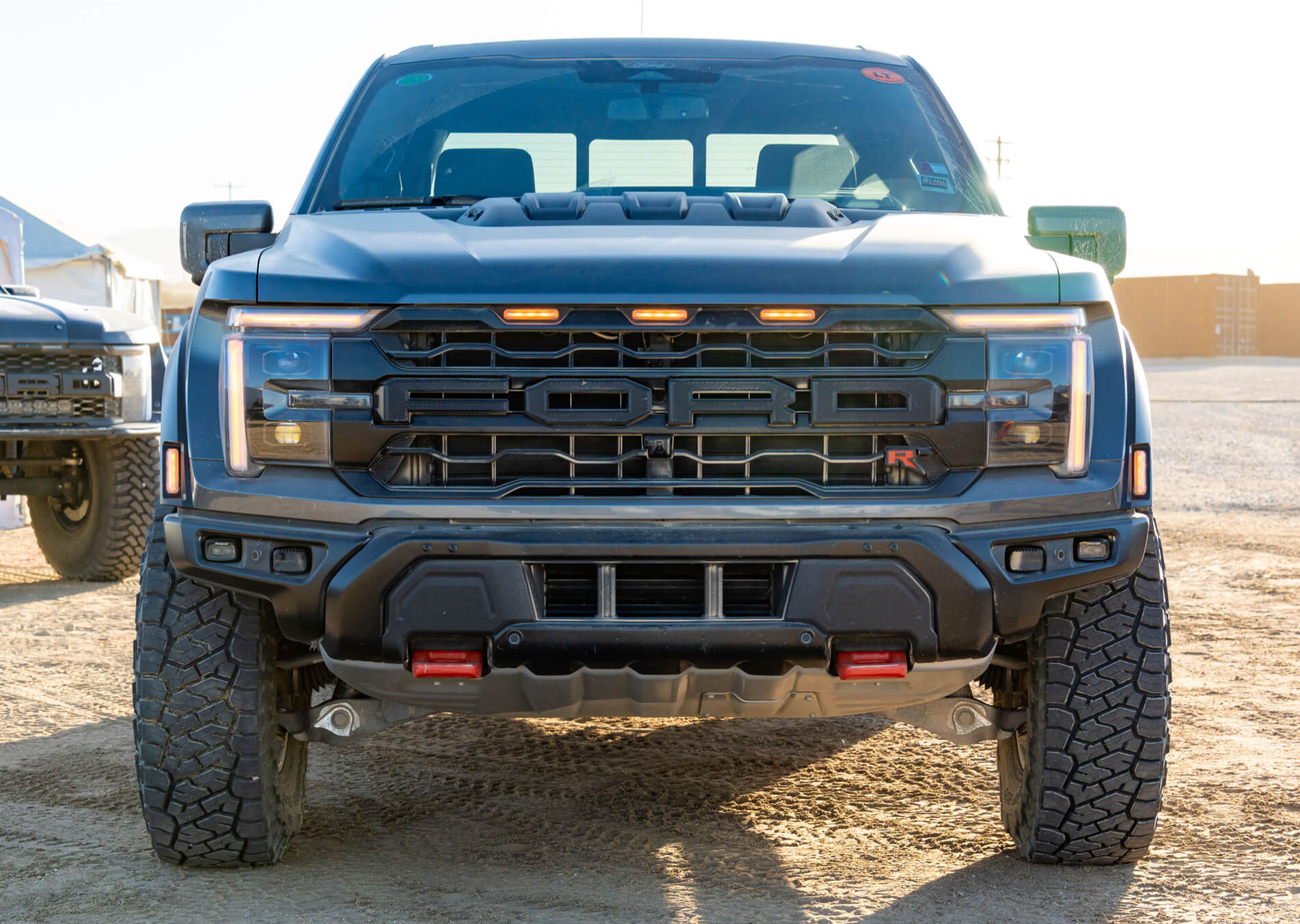 Ford truck with large grille and off-road tires on a dirt road.