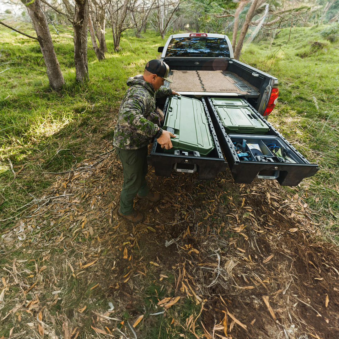A man in a camo jacket pulling a Ranger Green D-co case out of his DECKED Drawer System.