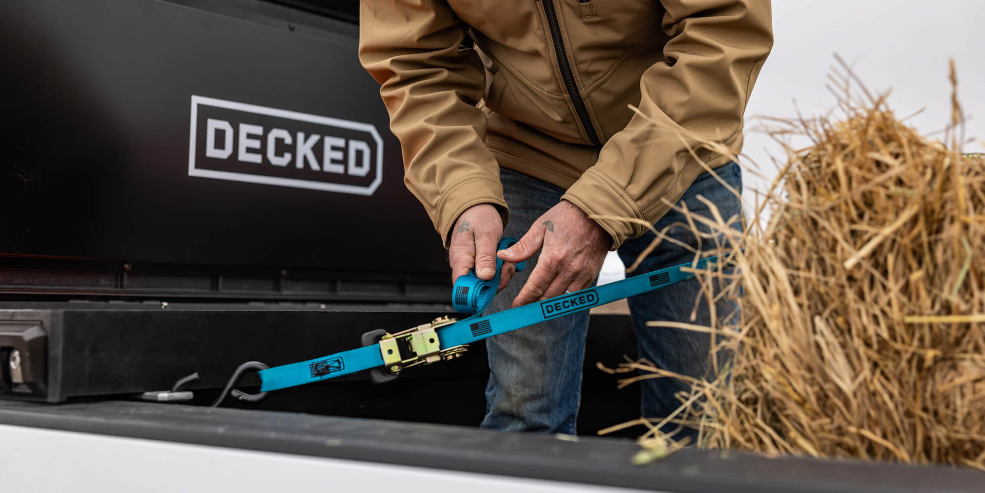 Person securing a bale of hay with a blue strap next to a DECKED'Tool Box.