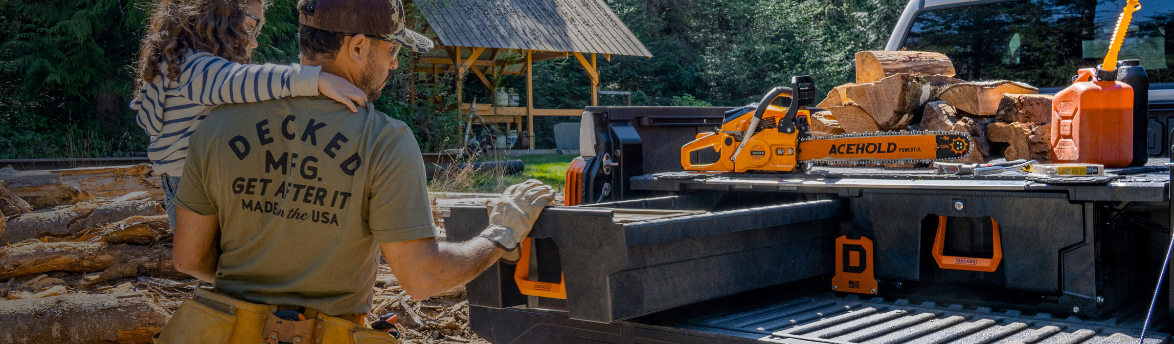 A dad and his daughter putting tools away into his DECKED Drawer System with orange Hop Up Kit handles in a wooded area with a truck bed filled with logs and equipment.