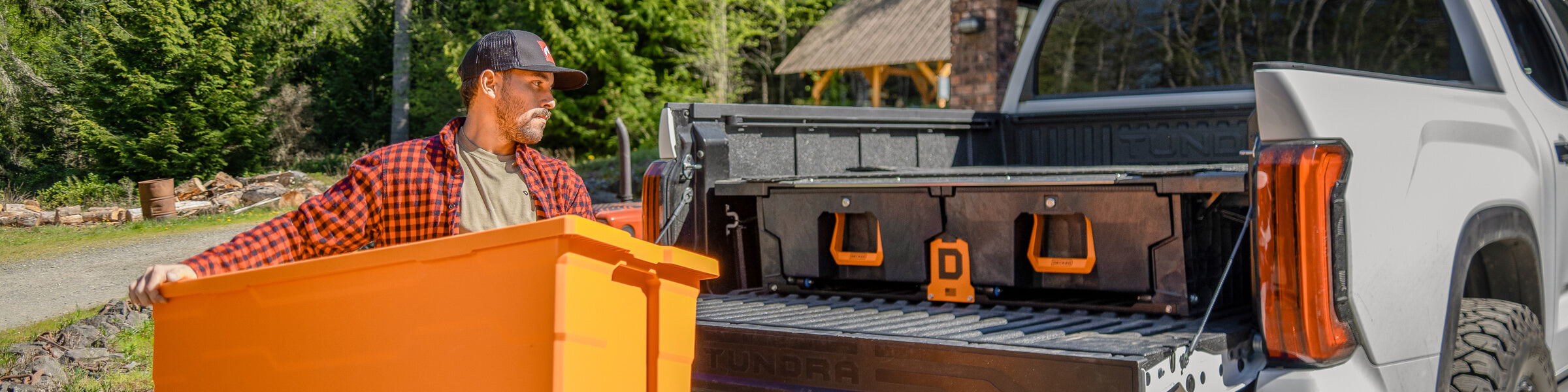 A man loading a large orange Payloader 133 Bin into the back of his truck bed that has a DECKED Drawer System inside.
