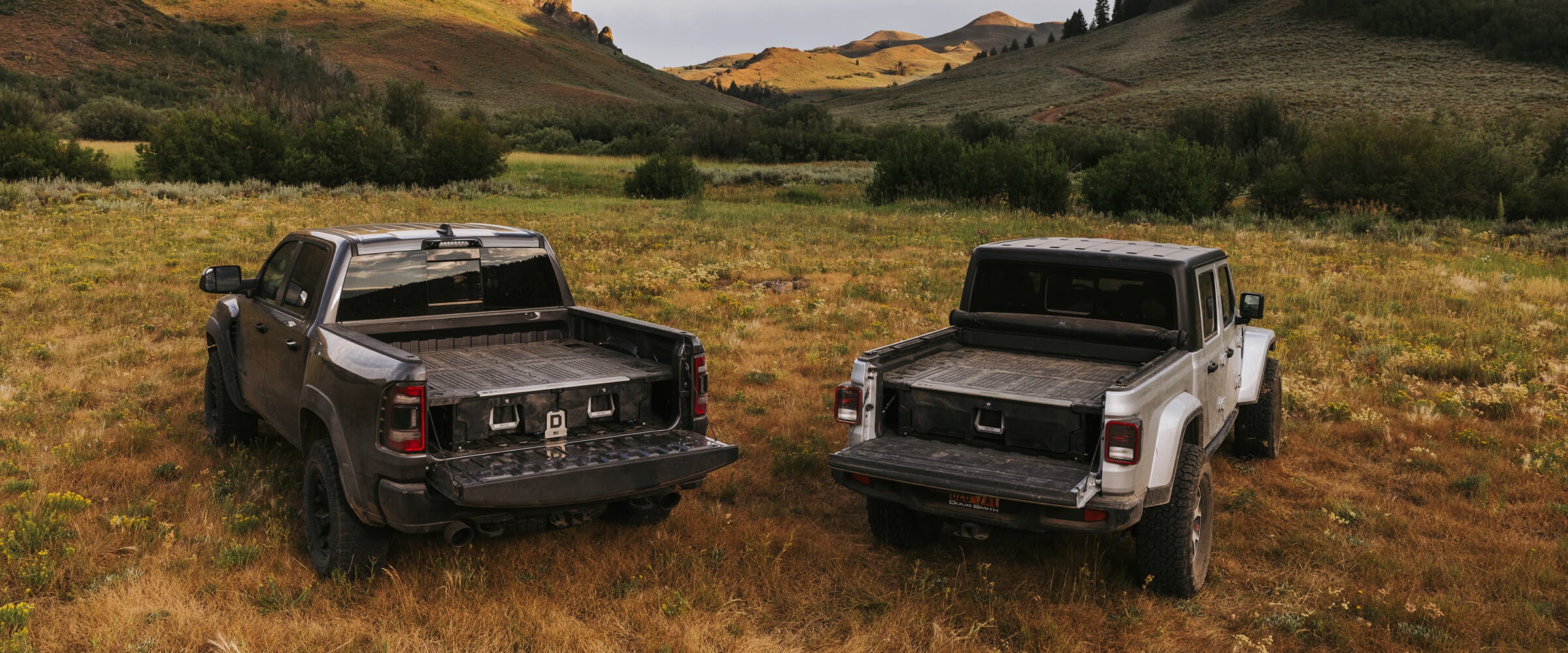 Two trucks parked in the mountains with drawer systems inside.