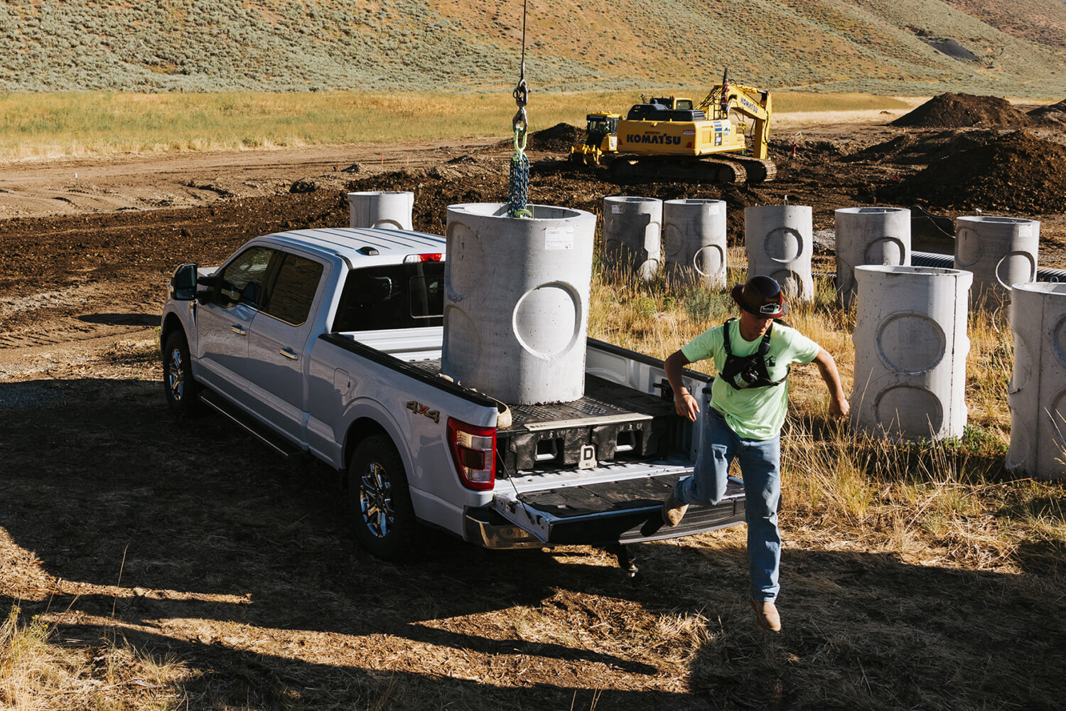 A construction worker stepping off of his tailgate after loading a cement cylinder onto the top of his drawer system.