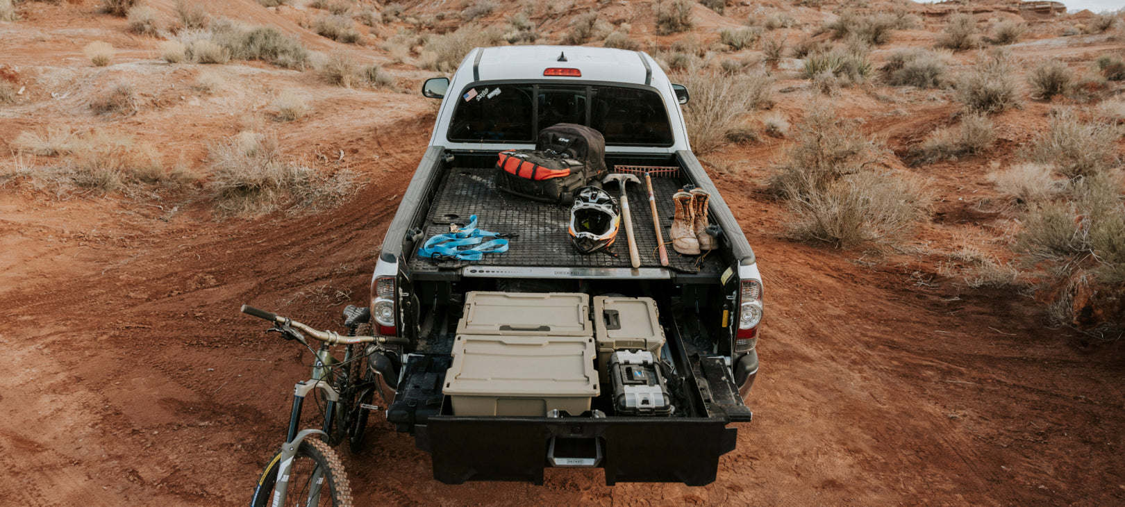 An open Drawer System in a midsize truck in the desert with bike gear organized in D-co Cases in the drawer and on the deck.