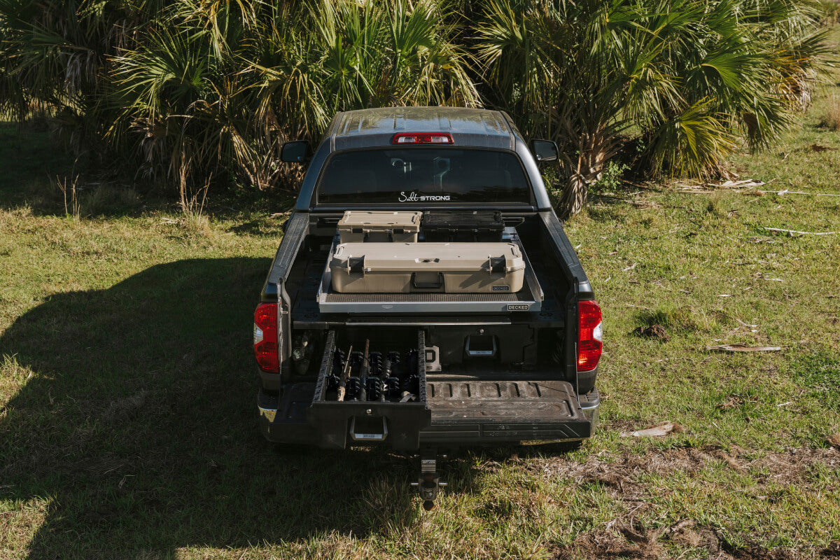A truck parked in front of palm trees, sporting a DECKED Drawer System, compatible CargoGlide, and three D-co Cases.