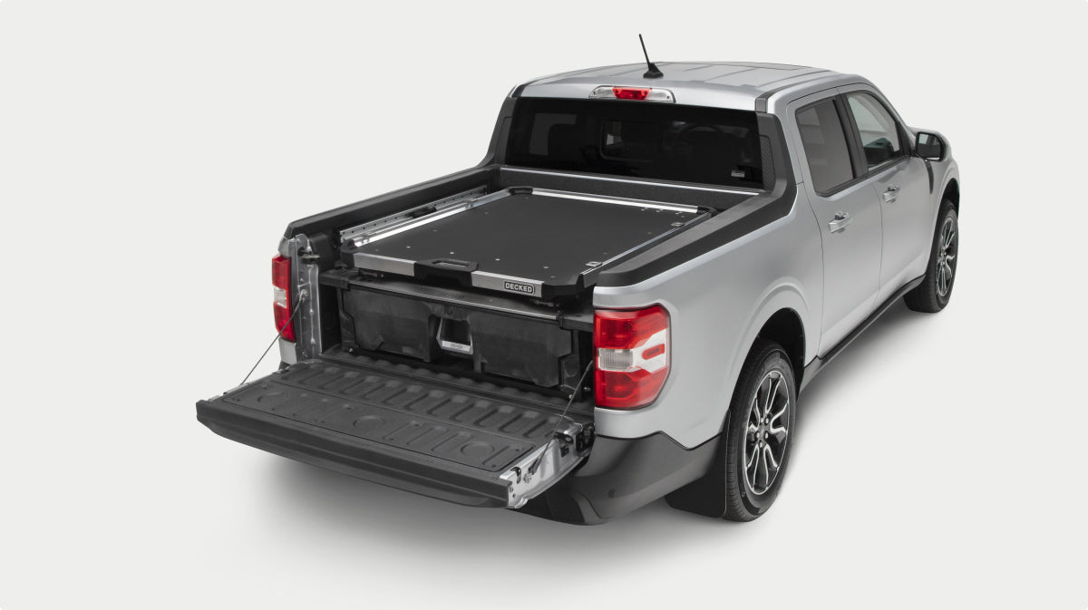A silver pickup truck shown from a rear three-quarter angle on a light gray studio background, with the tailgate open and a Drawer System and CargoGlide installed in the truck bed.