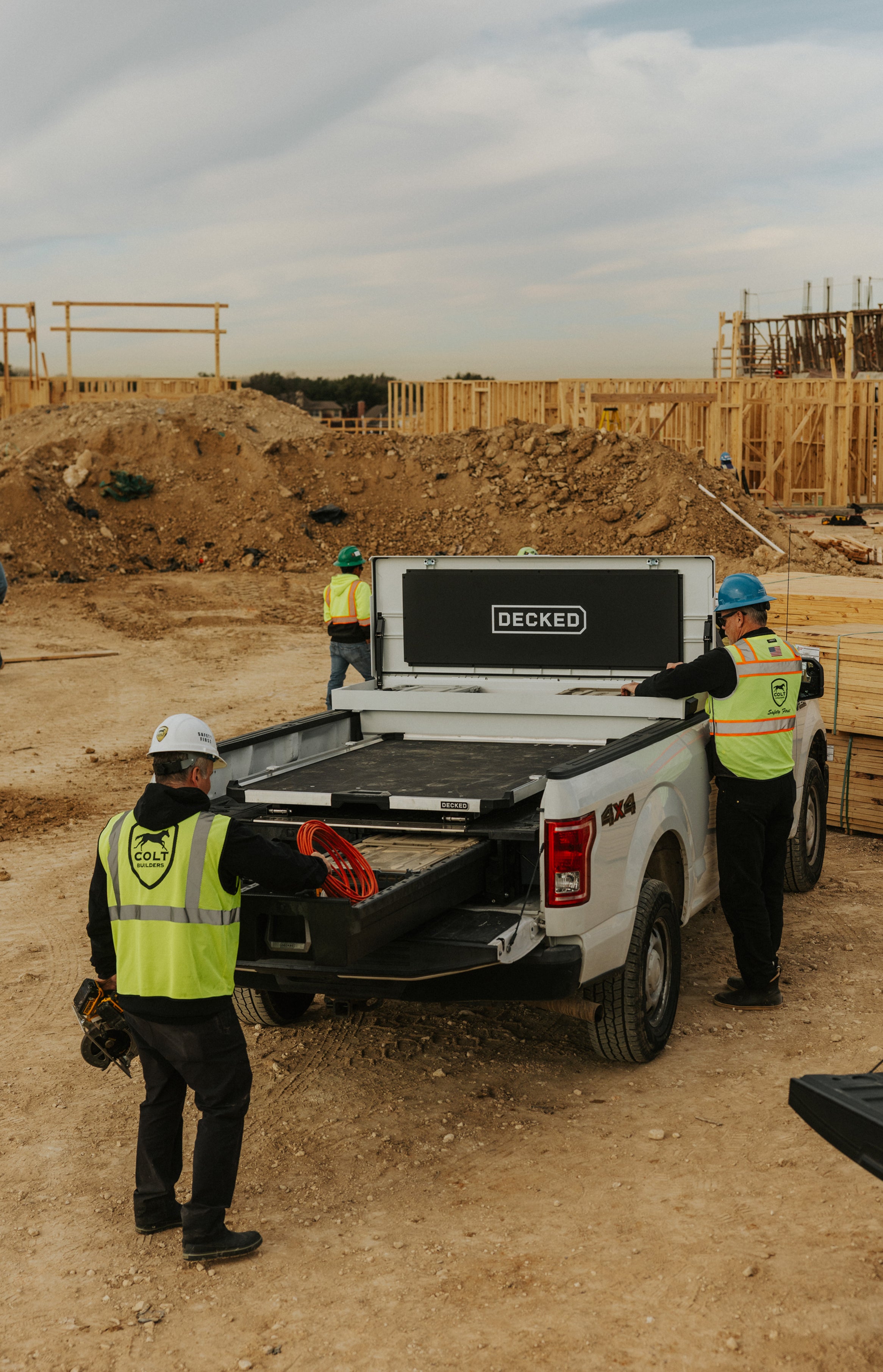 Three construction workers near a white truck with 'DECKED' systems at a construction site.
