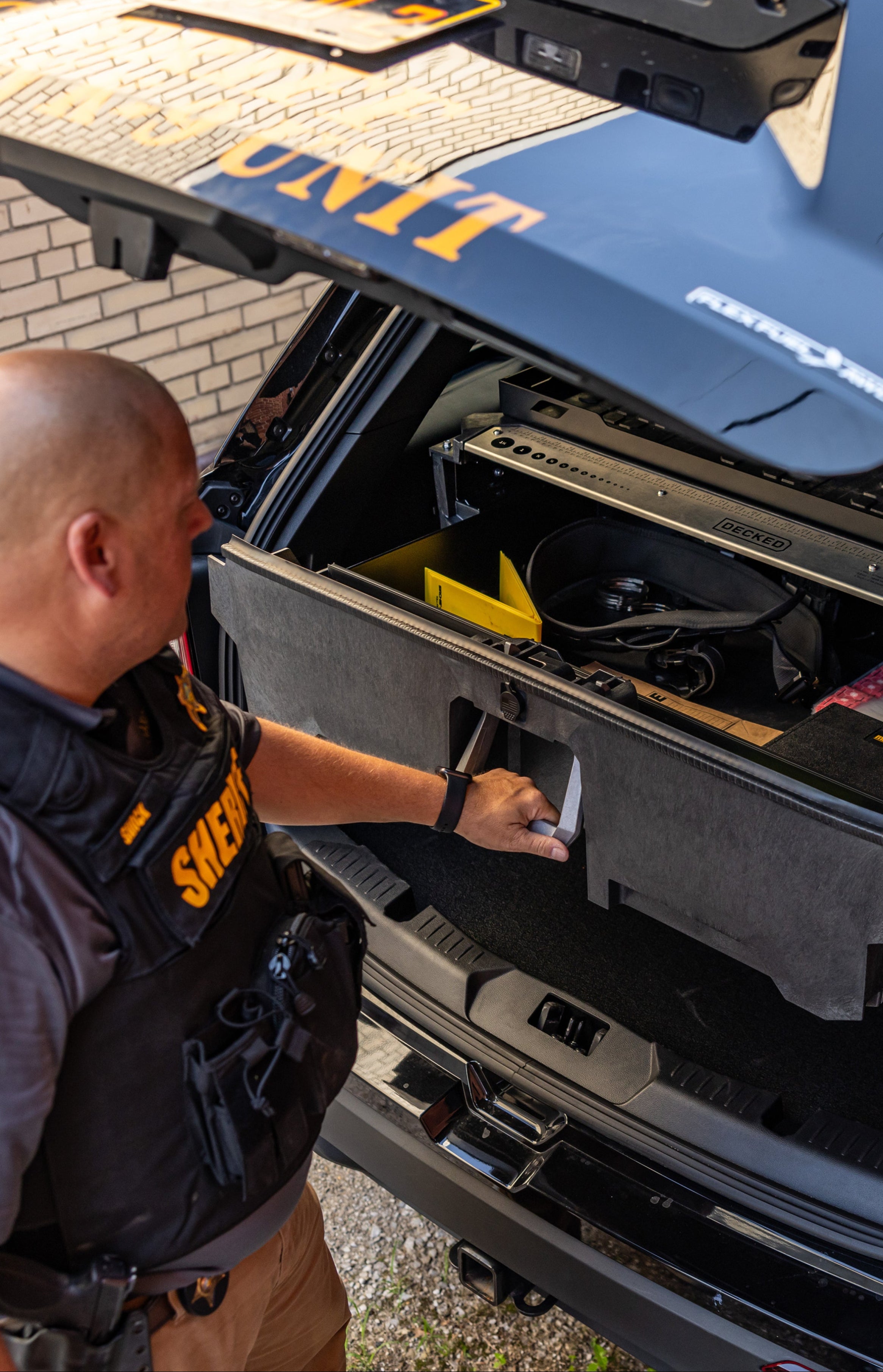 Person in a sheriff's uniform accessing storage compartments of a vehicle.