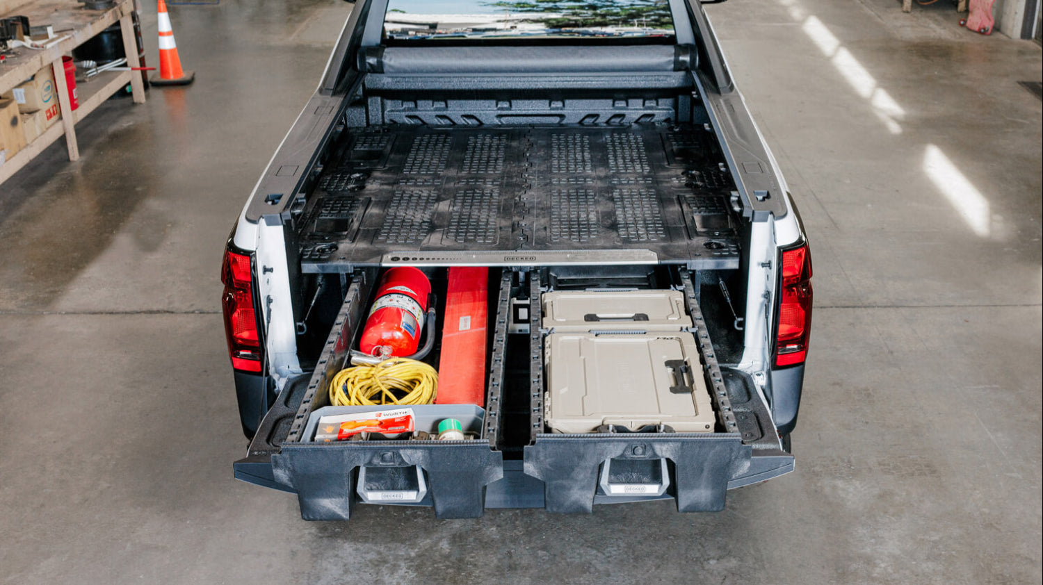 Truck bed with storage Drawer System open, showing tools and equipment on a concrete floor.