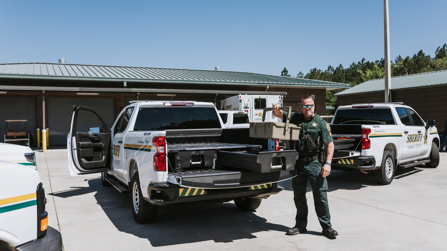 A Sherriff standing next to a white utility truck with open tailgate with Drawer System inside the bed in a parking lot.