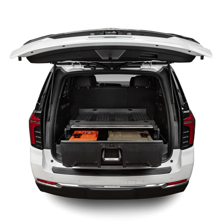 Rear cargo view of a white Chevrolet Tahoe PPV with liftgate open, showing the DECKED Drawer System installed with the drawer extended and an orange tool case and tan bin inside.