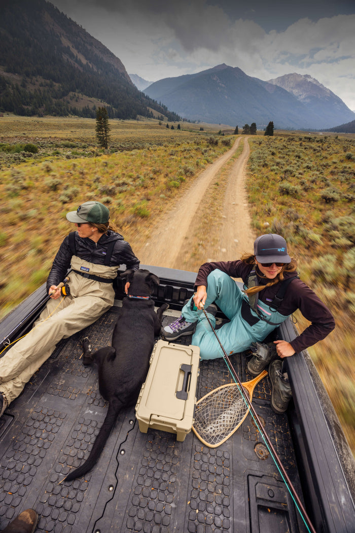 Two women in fishing waders and a dog in the back of a truck sitting on a DECKED drawer system on a two track road