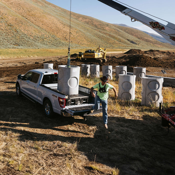 A contractor hopping off his tailgate while a crane lowers a concrete piling into his truck bed on top of a DECKED Drawer System.