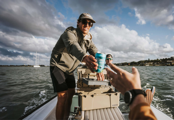 A guy on a fishing boat handing off a beer to his buddy as he pulls his tackle out of a DECKED D-CO case.