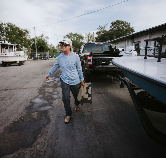 A woman at the boat launch carrying a DECKED D-Co case away from her truck that is towing a sleek salt water fishing boat.