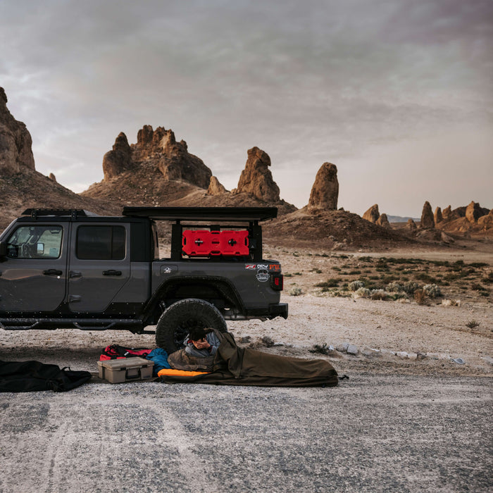 A no-frills camper in his sleeping bag next to his DECKED-out Jeep Gladiator in the middle of the desert.