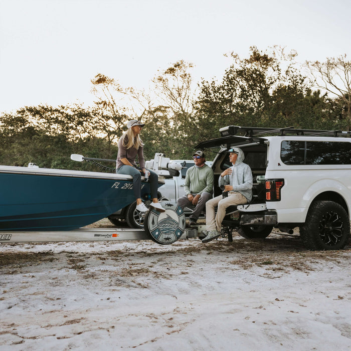 Three friends sitting on a tailgate with a DECKED system in the bed of the truck and a boat hitched up and ready to roll.