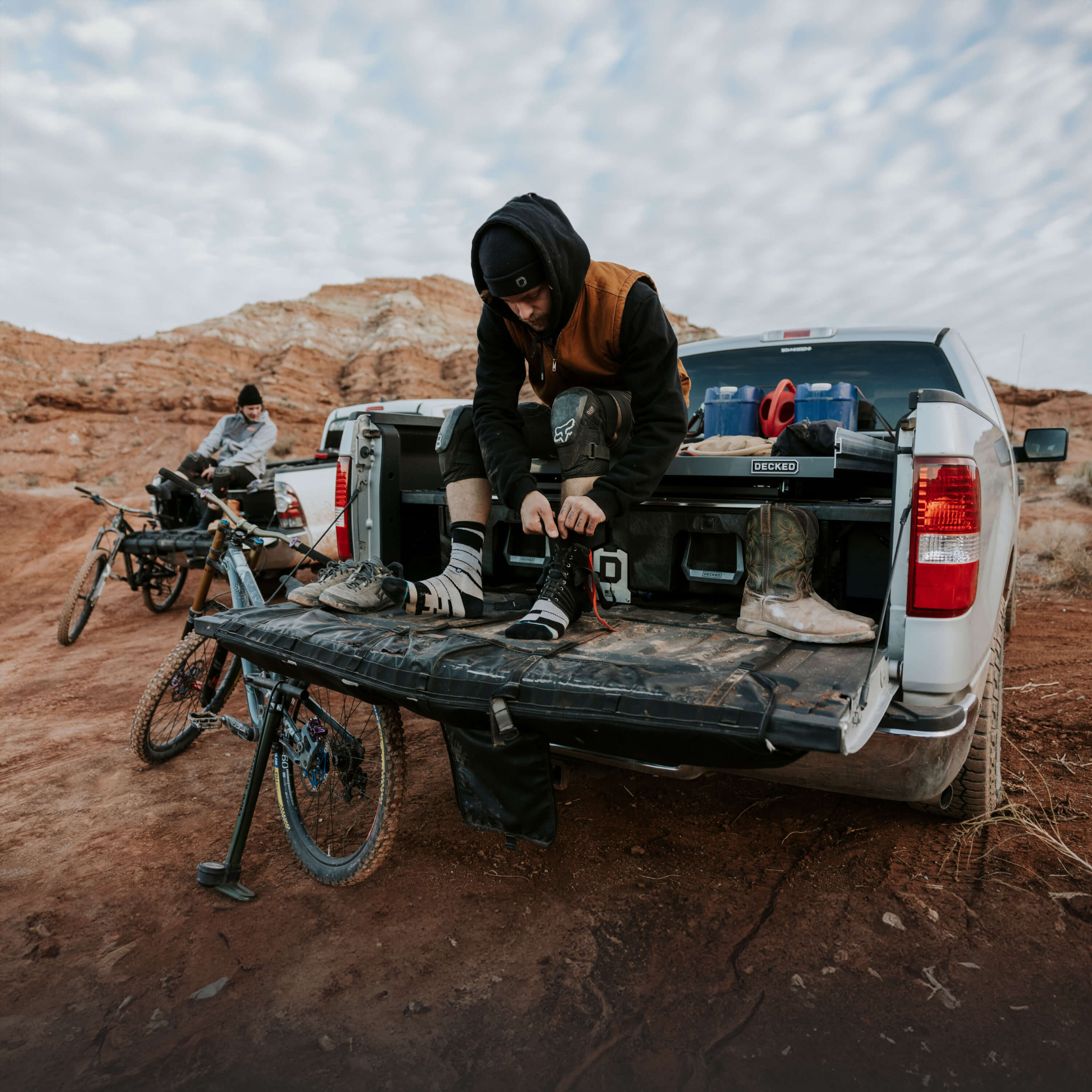 A mountain biker sitting on top of his DECKED Drawer System with the tail gate dropped, changing shoes in anticipation for his ride in the red rocks.