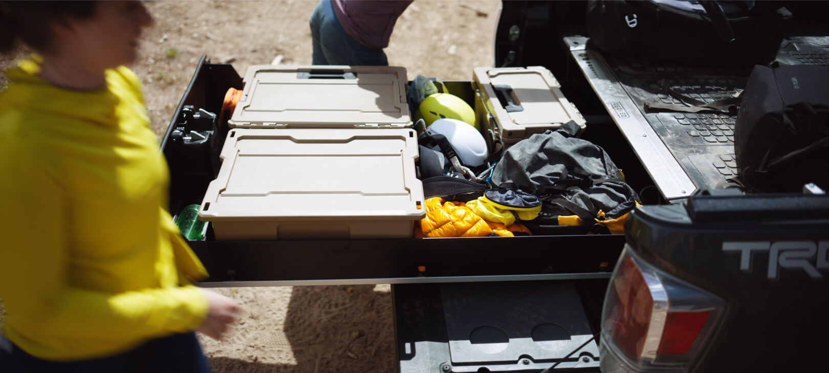 Two climbers working around their DECKED Drawer System which holds D-Co cases and well-organized climbing helmets, ropes and other gear.