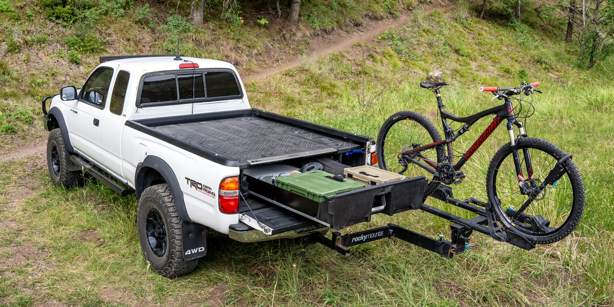 A white Gen 1 Tacoma with a bike trailer attached, parked on a dirt road with a Drawer System in the truck bed.