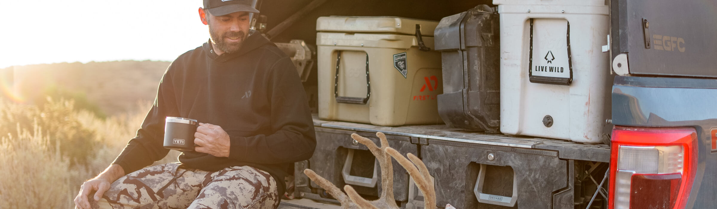 Remi Warren sitting on his tailgate in front of his Drawer System, coolers, and D-co case admiring deer antlers, still in velvet.