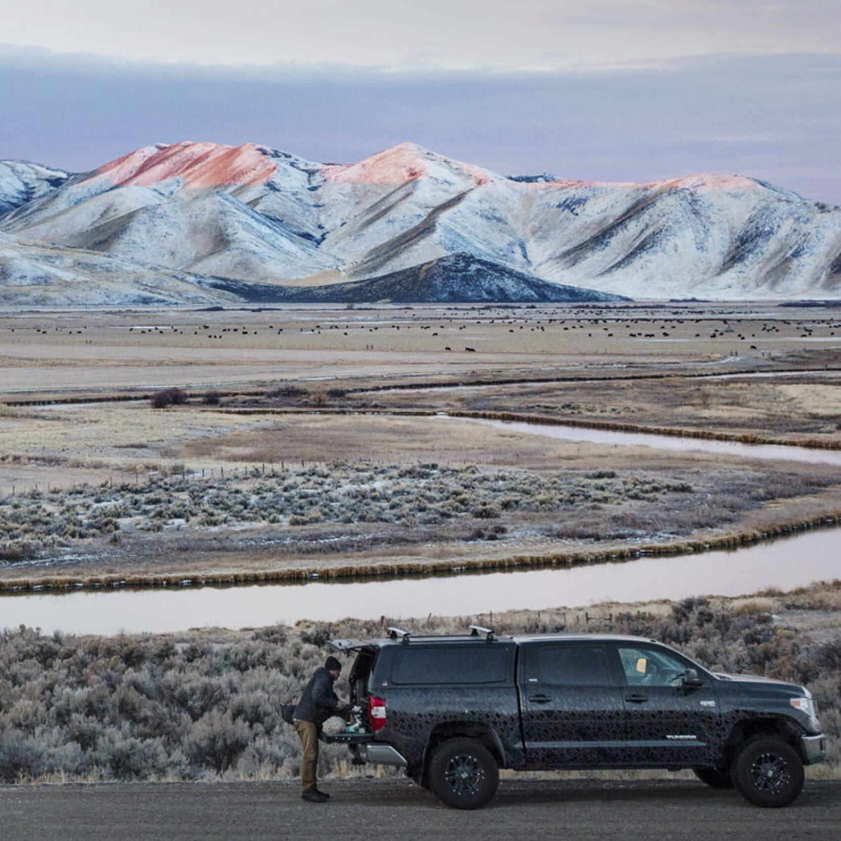truck parked next to a creek with mountains in the background