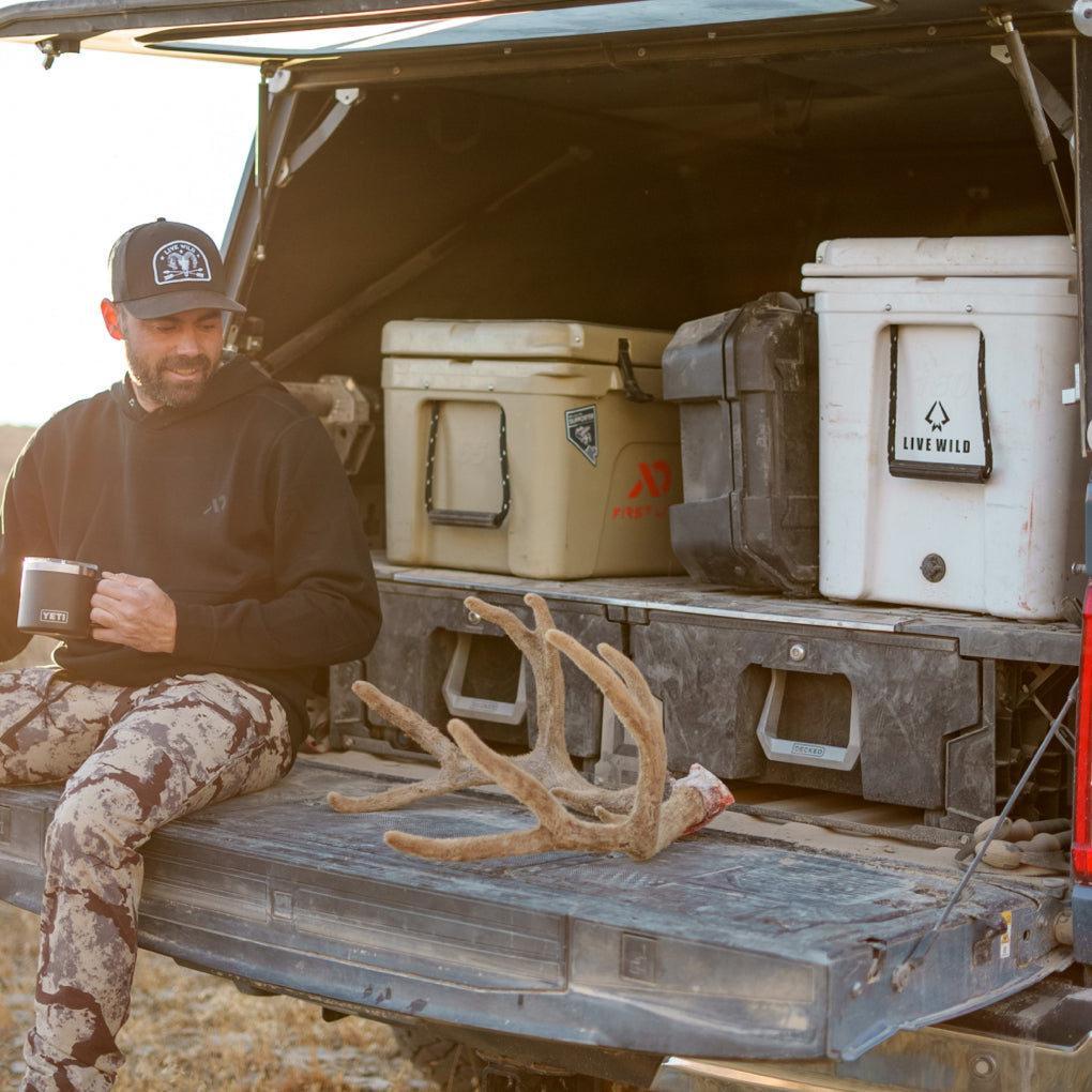 Remi Warren sitting on his tailgate in front of his Drawer System, coolers, and D-co case admiring deer antlers, still in velvet.