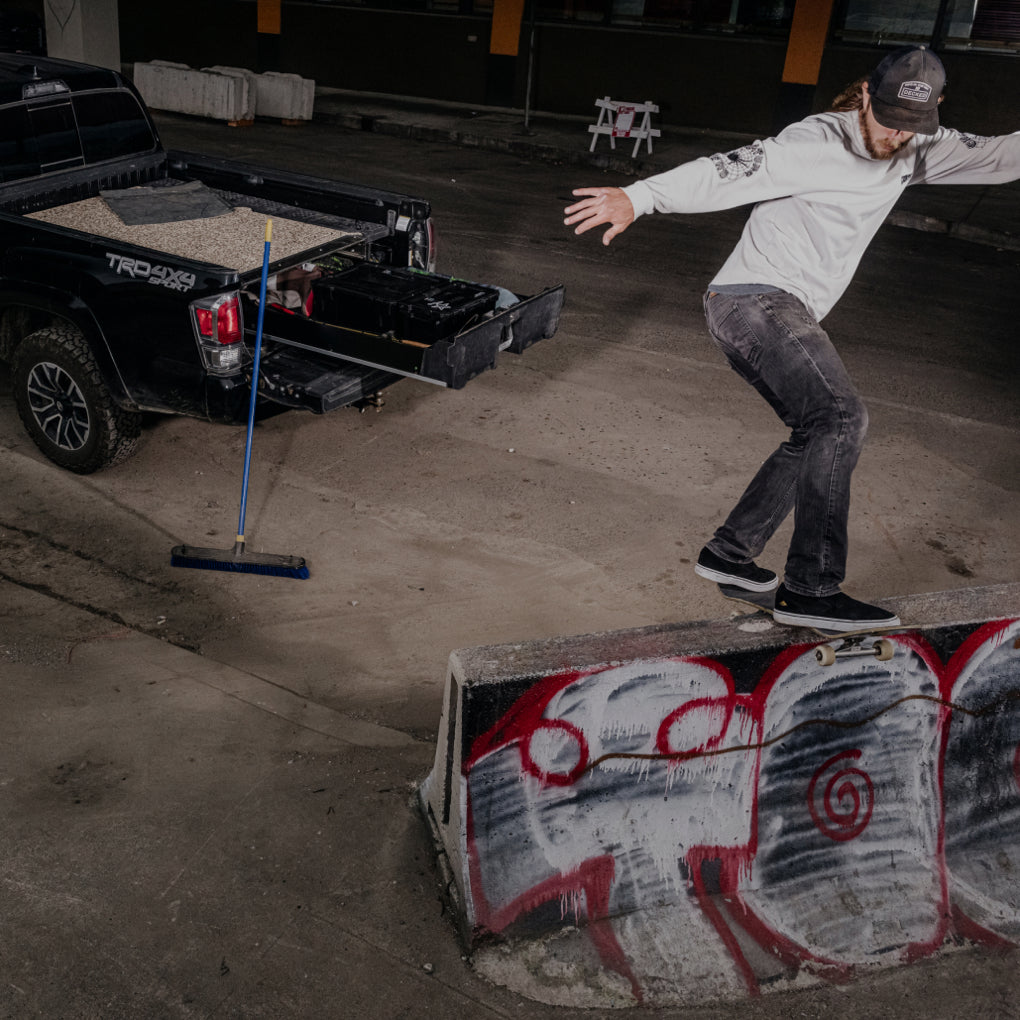 David Gravette performing a trick on his skateboard with his truck and Drawer System close by.