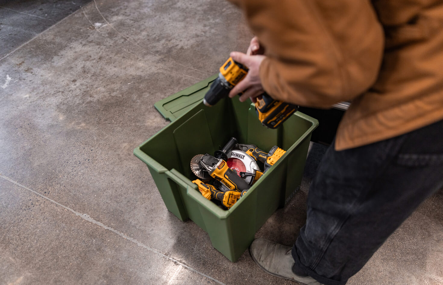 Person placing a power tool into a green Payloader 64 storage bin on a concrete floor.