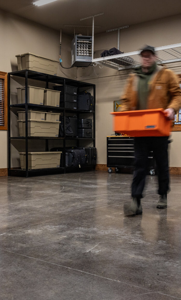 Person carrying an orange Payloader bin in a storage room with shelves and various sizes of DECKED cases and bins.