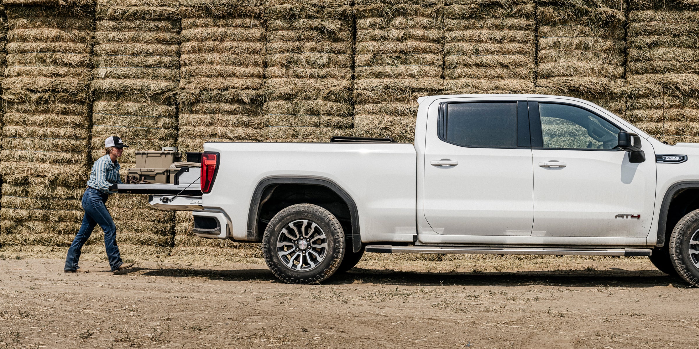 A woman rancher pushing her CargoGlide back into her truck bed - in the background is a wall of hay bales, piled high.