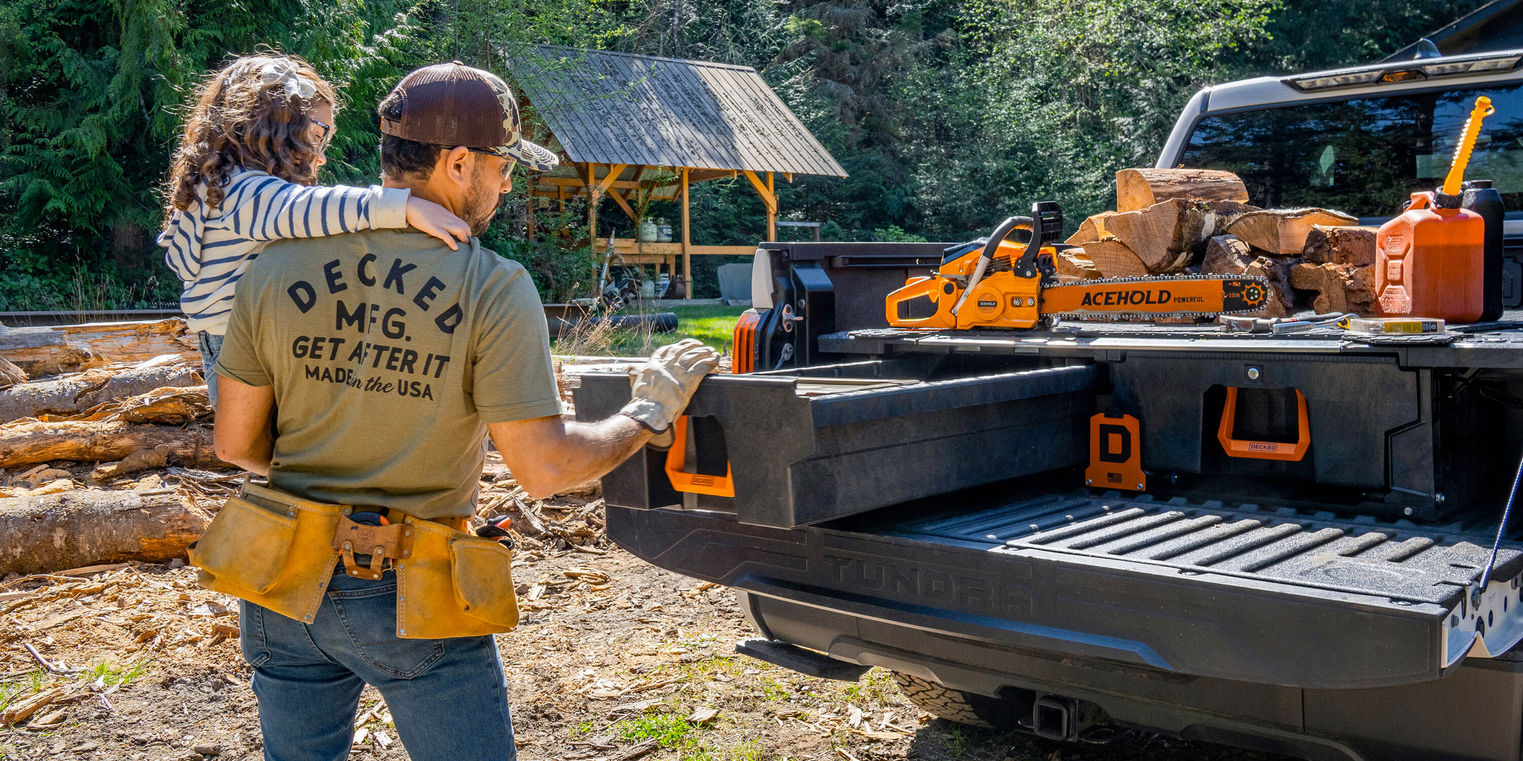 A dad and his daughter working with tools in a wooded area, with a truck bed filled with a DECKED Drawer System with orange handles.