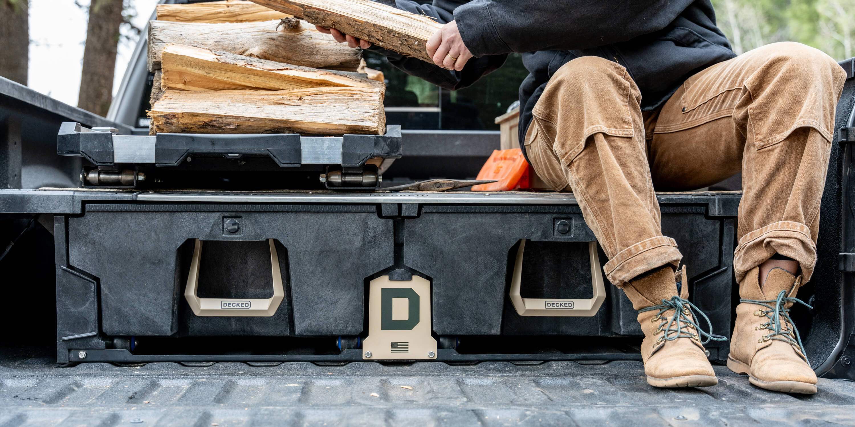 An image of a man in work boots sitting on his Drawer System that is equipped with the exclusive Desert Tan Hop Up Kit, the man is stacking cut wood on his CargoGlide 600.