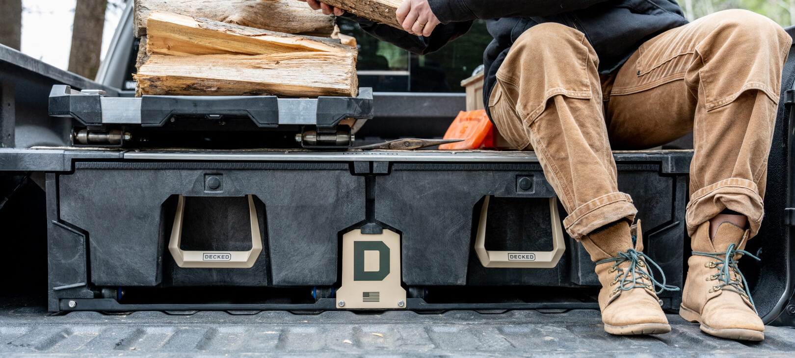 An image of a man in work boots sitting on his Drawer System that is equipped with the exclusive Desert Tan Hop Up Kit, the man is stacking cut wood on his CargoGlide 600.