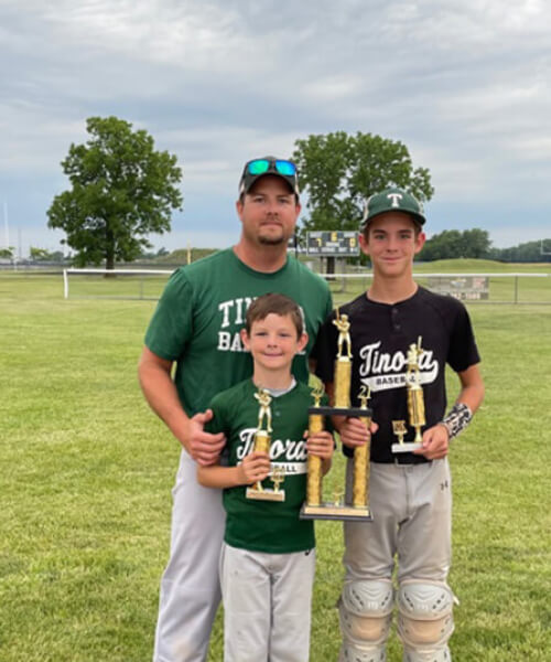 Man posing with two boys holding baseball trophys