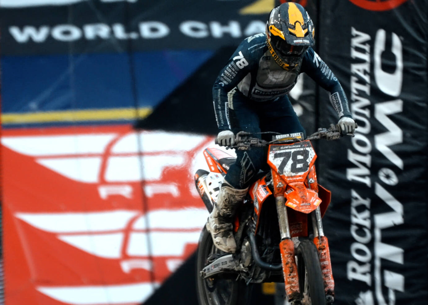 Supercross rider, Kevin Moranz, on an orange bike with number 78, wearing a helmet and goggles, against a branded background.