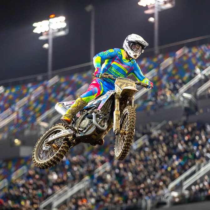 Supercross rider, Kevin Moranz, performing a jump during a race with a colorful bike and attire.