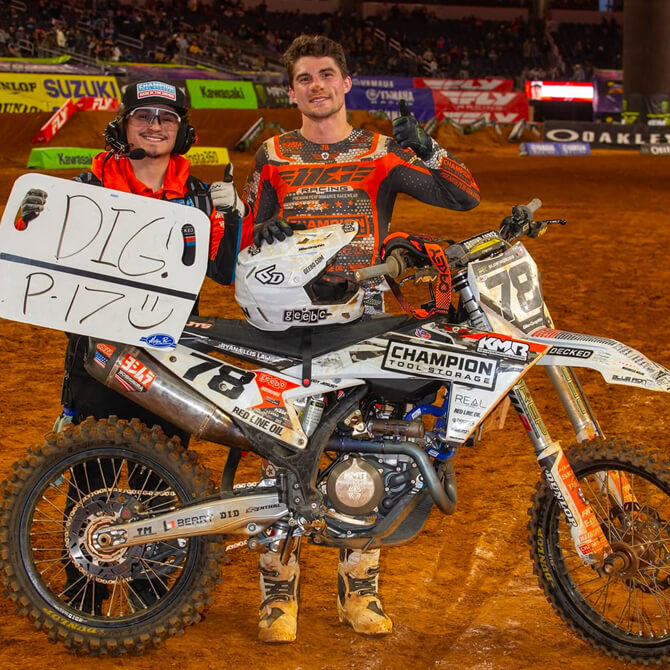 Kevin Moranz and his teammate posing with a bike on a track, holding a sign.