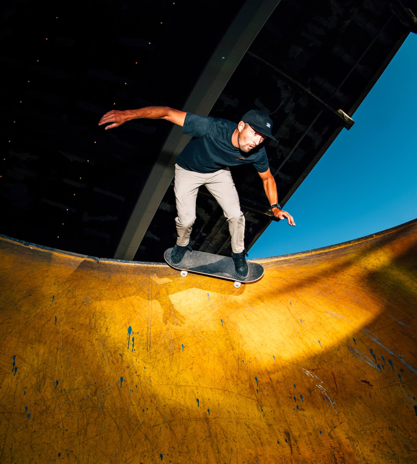 Skateboarder performing a trick on a half-pipe with a clear blue sky in the background