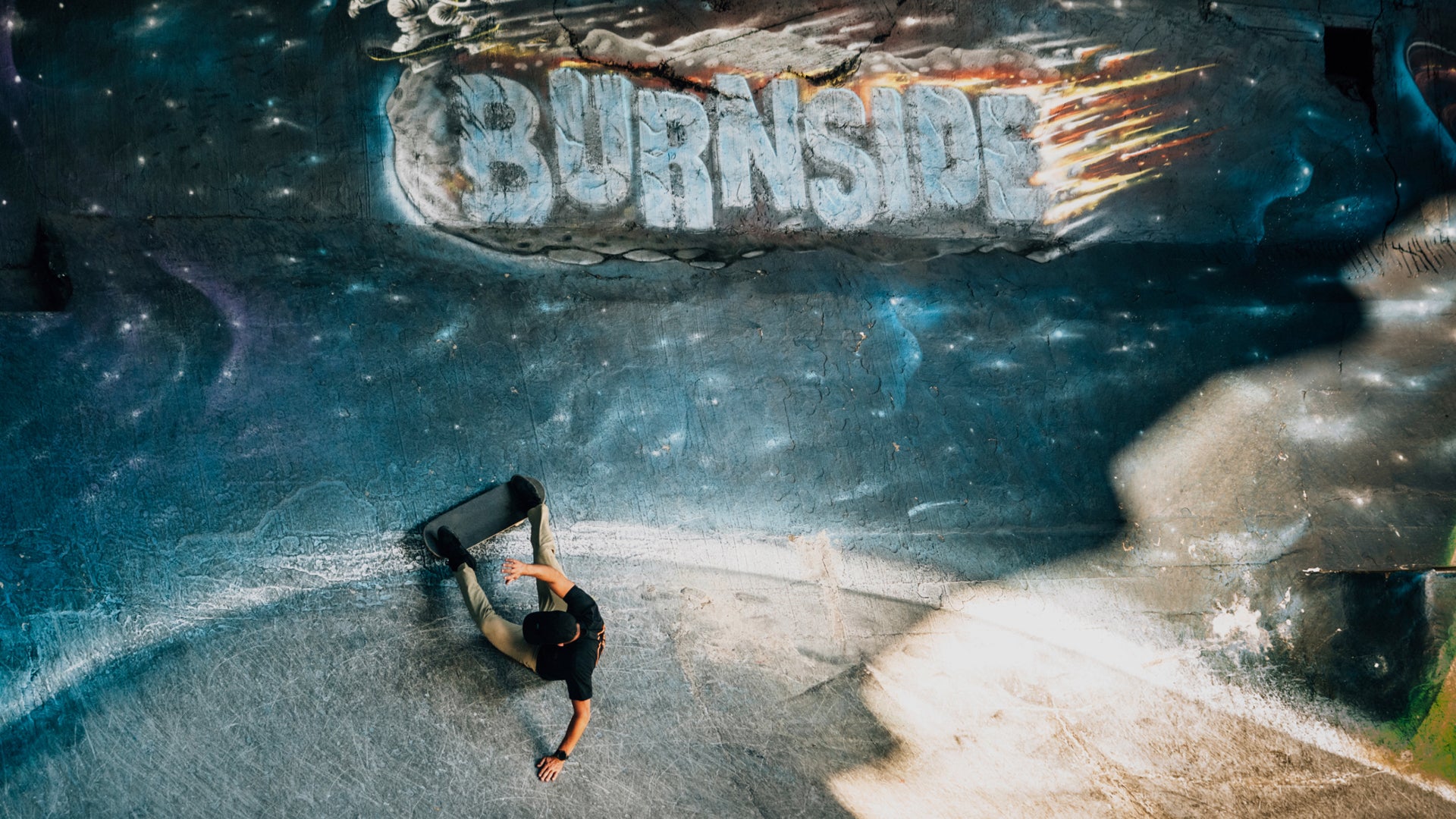 Person skateboarding in a bowl with 'Burnside' graffiti.