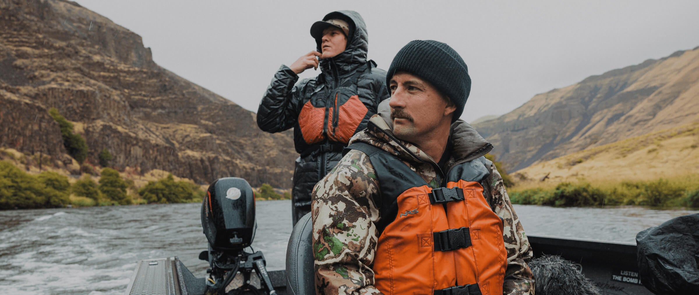 Two people in a boat on a river with mountains in the background