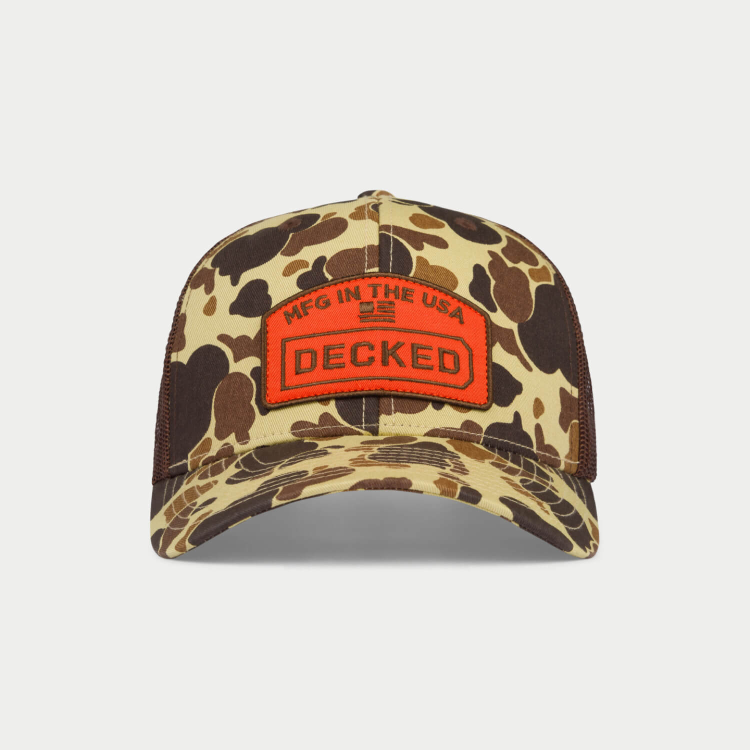  [H0112-HATR-CMO]  A green and brown camo hat with a mesh back with an orange badge on it that has an embroidered "MFG in the USA", American Flag, and DECKED logo.