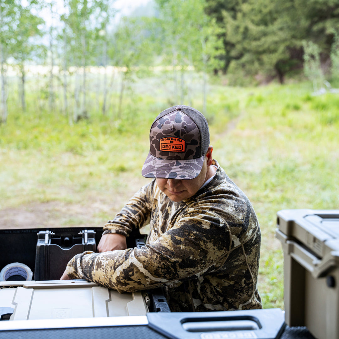 A camo hat with a mesh back with an embroidered "MFG in the USA" badge on a man.