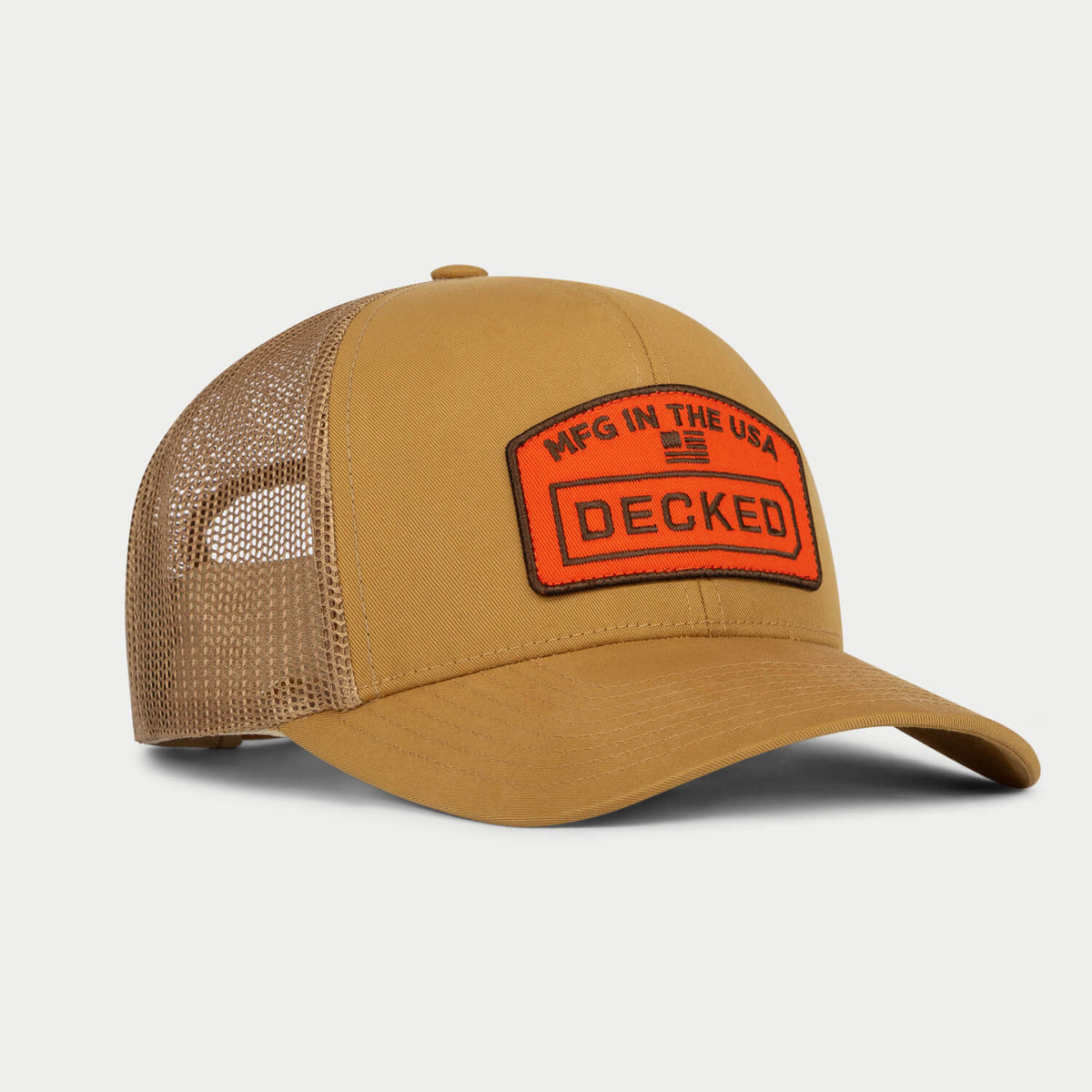 [H0777-TMFG-CYT] Three-quarter view of a coyote-tan trucker hat with an orange patch reading 'MFG in the USA' above the DECKED logo.