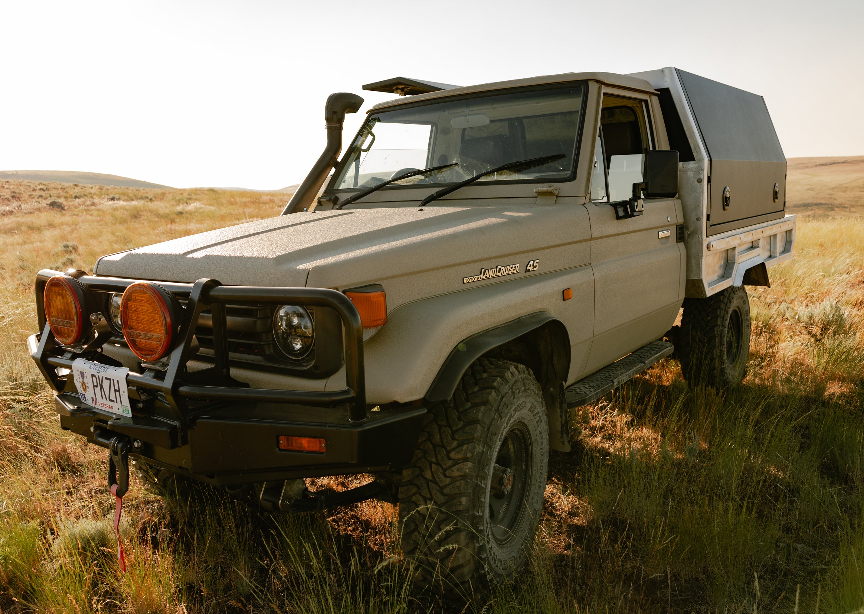 1999 Toyota Land Cruiser 4.5 equipped with a DECKED storage system, parked in a grassy field with rolling hills in the background.